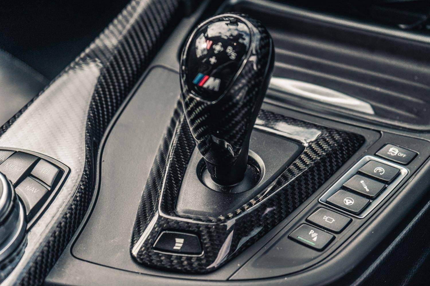 Close-up view of a car's gear shift lever and control buttons in a carbon fiber console.